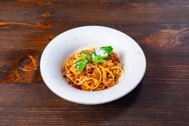 Çıtır ekmek kırıntıları ve taze otlarla kaplı leziz spagetti ahşap bir masada kırsal bir kasede sergileniyor ve sıcak ve davetkar bir yemek deneyimi yaratıyor..