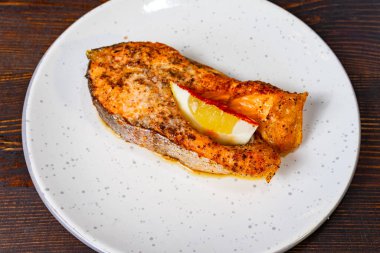 Tavada kurutulmuş somon filetosu bir dilim limonla süslenmiş beyaz bir tabakta sunulur. Tabakta altın bir kabuk var. Lezzetli bir çeşni. Sağlıklı bir yemek için ideal..