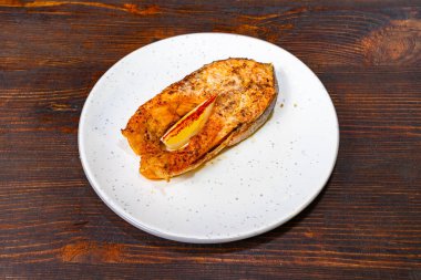 Mükemmel ızgara somon bifteği bir dilim limonla süslenmiş beyaz bir tabağa konur. Tabakta altın-kahverengi bir kabuk ve yumuşak bir doku var..