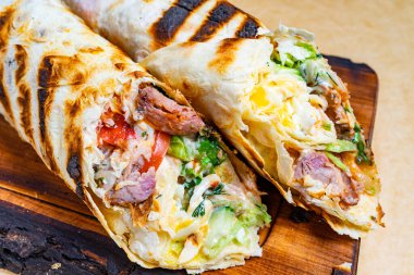 Taze sebze, et ve sos gibi çeşitli malzemelerle dolu ızgara paketler ahşap bir tahtada sunuluyor, iştah açıcı dokular ve renkler sergileniyor..