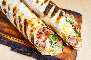 Ahşap bir tahtanın üzerinde, canlı sebze ve et dolu iki ızgara ambalaj sergileniyor. Paketler mükemmel bir şekilde kızartılmış, iştah açıcı bakışlarını vurguluyorlar..