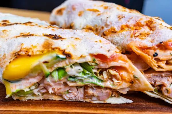 İki lezzetli paket, ahşap bir kesim tahtasının üzerinde ızgara et, taze sebze ve zengin soslar gibi canlı malzemeler sergiliyor. Hızlı ve tatmin edici bir yemek için mükemmel..