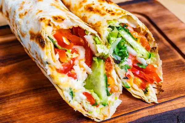 Renkli bir ambalajda domates, marul ve salatalık gibi taze sebze katmanları yer alır. Ahşap bir tahtada sunulan yemek iştah açıcı ve sağlıklı görünüyor..