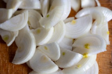 Beyaz soğanlar ince dilimlenmiş ve ahşap bir kesme tahtasına yerleştirilmiş. Parlak dokuları ve taze görünüşleri sergileniyor. Çeşitli yemeklere tat katmak için mükemmel..