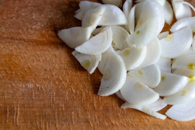 Taze beyaz soğanlar ince ince dilimlenir ve ahşap bir kesme tahtasına yerleştirilir. Mutfak ortamında yemek ya da yemek tarifi hazırlama öneriliyor. Mutfak etkinliği vurgulanıyor.