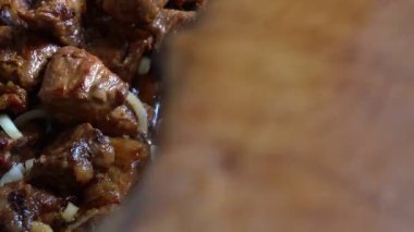 Zengin bir sosta yumuşak et parçaları marine edilirken, doğranmış soğanlar lezzeti artırmak için ekleniyor. Yemek sıcak bir mutfakta hazırlanıyor, yemek pişirmek için davetkar bir ortam yaratıyor..