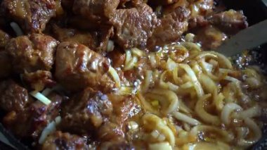 Bol soslu taze et parçaları, karamelli soğanla çevrili bir tavada. Yemek, doyurucu tatlar ve rahatlatıcı kokular sunuyor. Tatmin edici bir yemek için mükemmel..