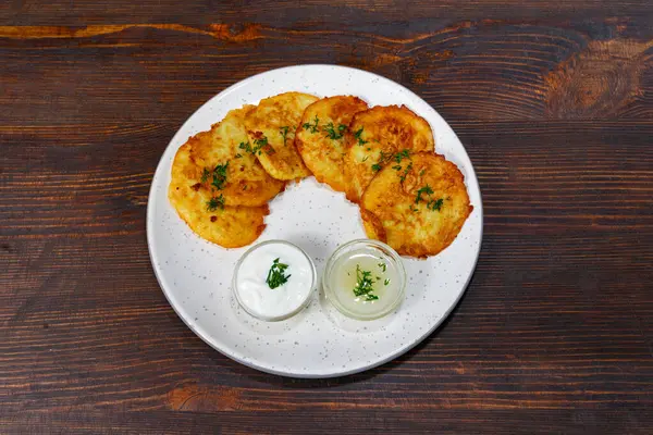 Bir tabak altın rengi patatesli krep taze otlarla süslenir. İki küçük kase yoğurt ve ekşi krema tabağa eşlik ederek kremalı bir kontrast ekliyor..