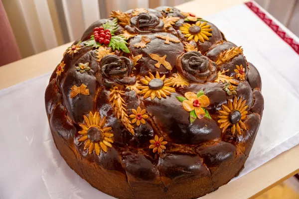 Yuvarlak bir bayram ekmek sergisi hamurdan yapılmış çiçek süslemeleri ve tasarımları karmaşıklaştırır. Sergide ayçiçekleri, güller ve böğürtlenler, özel günler için uygun canlı ve neşeli bir görünüm sunuluyor.