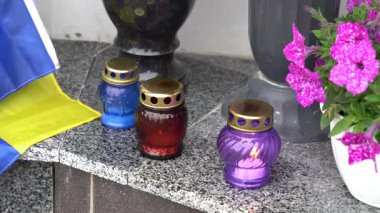Ukrayna 'daki bir anma töreninde çeşitli renkli mumlar yakılıyor, canlı çiçekler ve bir bayrak eşliğinde, burada hatırlananları onurlandırmak için dingin bir anma töreni düzenleniyor..