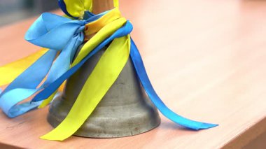 Geleneksel bir çan, mavi ve sarı kurdelelerle süslenmiş tahta bir yüzeyde bulunur. Bu, Ukrayna 'da bir festival vesilesiyle eğitim kutlamalarını sembolize eder ve öğrencileri karşılar..