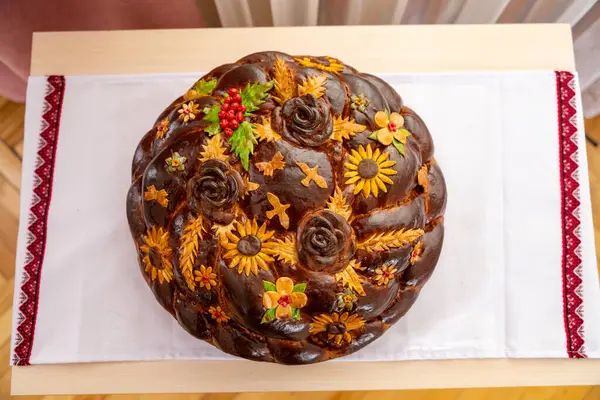 Karmaşık tasarlanmış yuvarlak bir somun ekmek vitrinleri renkli çiçek desenleri ve yaprak süslemeleri. Kültürel önemi vurgulayan kırmızı işlemeli beyaz keten kumaşa dayanır..