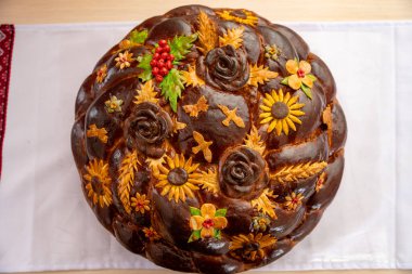 Karmaşık çiçekli ve yaprak tasarımlı renkli ekmek beyaz bir kumaşın üzerinde duruyor. Bu geleneksel ürün, yerel bir kutlama sırasında kültür mirası ve zanaatkarlığı yansıtıyor..