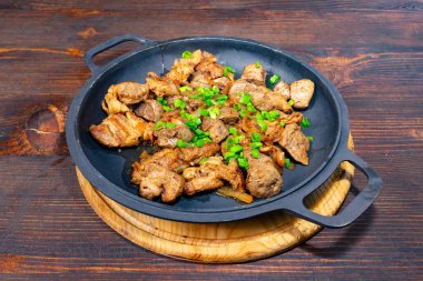 Lezzetli bir et yemeği taze yeşil soğanla süslenmiş siyah bir tavada cızırdıyor. Sıcak ahşap masa yemeğin davetkar atmosferini arttırır..