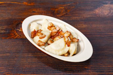 Patates ve peynirle dolu lezzetli hamur köfteleri gevrek domuz pastırması ile kaplanmış beyaz bir tabakta sunulur kırsal ahşap bir masada, iştah açıcı bir deneyim davet edilir..