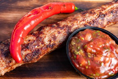 Sulu ızgara et şişleri yanında bir kase baharatlı salsa sosu ve üzerinde taze kırmızı biberle sunulur. Sıcak havalarda açık havada toplanmak için birebirdir..