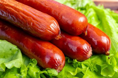 Sulu sosisler taze, taze marul üzerinde güzelce düzenlenir, renklerin kontrastını vurgular, yaz barbeküleri veya piknikler için idealdir. Lezzetli bir yemek için mükemmel..