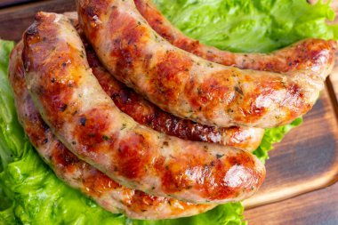 Altın-kahverengi kabuklu ızgara sosisler canlı yeşil marul üzerinde ustalıkla düzenlenir. Sıcak, kırsal ortam, arkadaşlarla geçirdiğimiz yaz barbekü atmosferini vurguluyor..