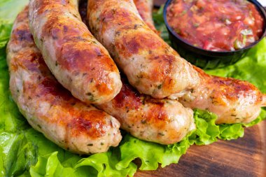 Kıtır marul yatağında altın-kahverengi kabuklu ızgara sosis. Bir kase taze salsa, iştah açıcı sunumu artırmak için canlı bir dokunuş ekler..