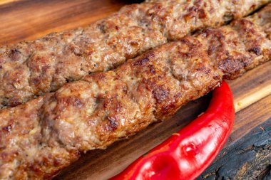 Sulu et şişleri, kahverengi bir dış görünüş sergileyerek mükemmelce kızartılıyor. Parlak kırmızı kırmızı biber, ahşap bir yüzeydeki lezzetli yemeğin yanına biraz renk katar..