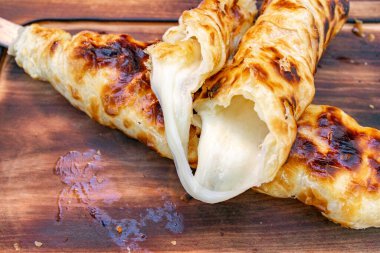 Eritilmiş peynirle dolu gevrek hamur külahları ahşap bir tabakta servis ediliyor ve festivaller sırasında açık hava marketlerinde sıklıkla beğenilen lezzetli bir sokak yemeği seçeneğini sergiliyorlar..