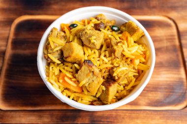 Lezzetli bir kase pirinç rengarenk sebzelerle birlikte mükemmel pişirilmiş tavuk parçaları. Tabak kırsal ahşap bir yüzeyde sunuluyor, davetkar niteliklerini sergiliyor..