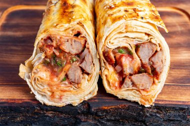 İki lezzetli paket ikiye bölünüyor, taze et ve canlı sebzeler sergileniyor, ahşap bir tahtanın üzerinde dinleniyor, aromaları ve dokuları renklendiriyor..