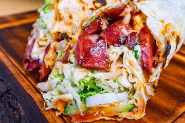 Ağız sulandıran bir burrito, canlı bir yemek atmosferinde kırsal ahşap bir tabakta servis edilen marul, lahana ve et gibi renkli malzemelerle dolup taşıyor..