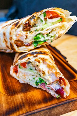 Izgara tavuk, çıtır sebze ve sosla dolu bir paket ahşap bir tahtanın üzerinde sergileniyor. Mutfak ortamında taze malzemeler sergileniyor..