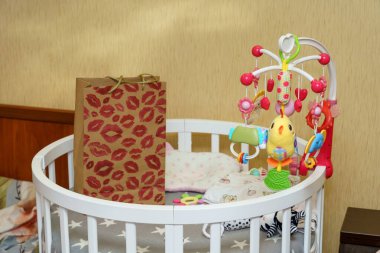 Rahat bir çocuk odasında oyuncaklarla süslenmiş bir beşik ve yakınlarda dinlenen dekoratif bir çanta bulunuyor. Renkli cep telefonu neşeli bir dokunuş ekliyor, hoş bir atmosfer yaratıyor..