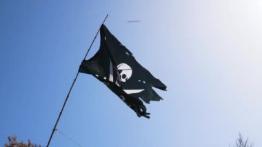 Tamamen parçalanmış ve morarmış siyah korsan bayrağı (Jolly Roger) rüzgarda dalgalanan bir bayrağa bağlanmış, kafatası yaması ve kumaşın üzerine beyaz çizilmiş iki kılıçla birlikte.