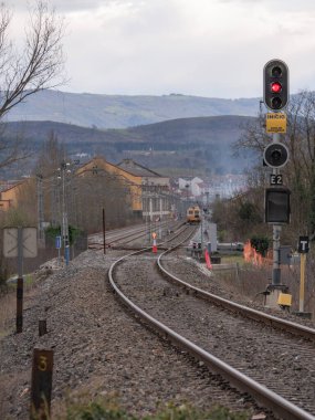 Monforte de Lemos, Lugo, İspanya; 03-21-2022; Monforte istasyonunun girişinde ışıklandırılmış sinyal elektrik işleri sırasında kırmızı (dur) göstermektedir ve raylarda çalışan bir atölye treni