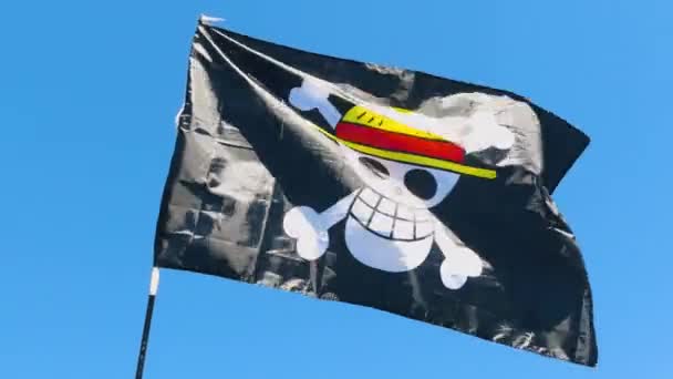 黒い海賊旗は 黄色いわら帽子と2つの白い骨に位置する赤いリボンを含んでおり 背景にマストと青い空に風を振っています — ストック動画