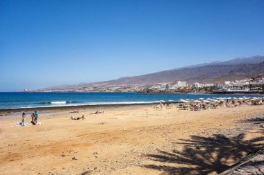 Arona, Tenerife, İspanya; 04-23-2024: Tenerife şehrindeki Playa de las Vistas, güneşlenen insanlar ve şemsiyeler ve Atlantik Denizi manzarası ile adanın manzarası