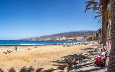 Arona, Tenerife, İspanya; 04-23-2024: Tenerife şehrindeki Playa de las Vistas, güneşlenen insanlar ve şemsiyeler ve Atlantik Denizi manzarası ile adanın manzarası