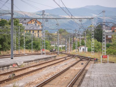 Ponferrada tren istasyonunun sonundaki platformun, alçak sinyallerin katenerin kabloları altında kırmızıyla aydınlatıldığı dağlara doğru gidişine bakın.