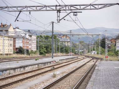 Ponferrada tren istasyonunun sonundaki platformun, alçak sinyallerin katenerin kabloları altında kırmızıyla aydınlatıldığı dağlara doğru gidişine bakın.