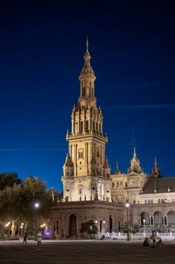 Sevilla, İspanya; 09 / 27 / 2024: Sevilla, İspanya 'daki Plaza de Espaa kulesi, gece aydınlandı. Koyu mavi gökyüzüne karşı zarif ve tarihi mimari