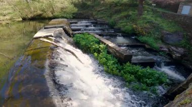 Nehir suyunun yapay bir basamaktan düşüşünü gösteren yavaş çekim videosu sıvıyı bir değirmene aktarmak için kullanılıyor.