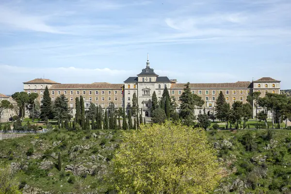 Toledo, İspanya; 04-09-2025: Toledo Piyade Akademisi panoramik görünümü, ağaçlar ve yeşillikler tarafından çerçevelenmiştir. Simetrik mimarisi ve merkezi kulesi olan görkemli tarihi bina.