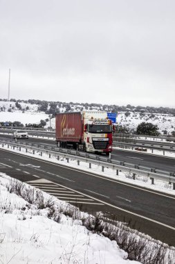 Guadalajara, İspanya; 03-16-2025: İspanya 'da karla kaplı A2 karayolu (Autovia del Nordeste) boyunca giden kamyon, kışın manzarası ve bulutlu gökyüzü ile çevrilidir. Soğuk hava lojistiği hareket halinde