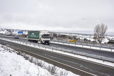 Guadalajara, İspanya; 03-16-2025: İspanya 'da karla kaplı A2 karayolu (Autovia del Nordeste) boyunca giden kamyon, kışın manzarası ve bulutlu gökyüzü ile çevrilidir. Soğuk hava lojistiği hareket halinde