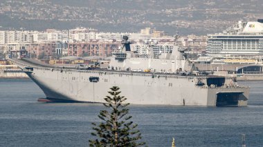 Malaga, İspanya; 07 / 07 / 2025: İspanyol donanmasının I. Juan Carlos uçak gemisi Mlaga limanına demirledi, şehir binaları ve yolcu gemisi arka planda gün ışığı altında