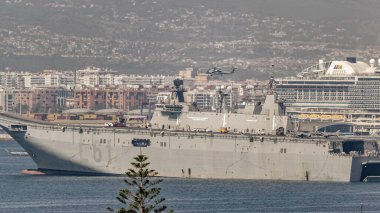 Malaga, İspanya; 07 / 07 / 2025: İspanyol uçak gemisi Juan Carlos I ile askeri helikopter ve yolcu gemisi Mlaga limanında. Şehir silüeti ve deniz manzarası Bu deniz ve sivil deniz manzarası