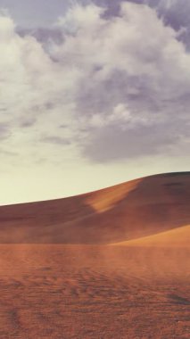 Issız kumlu çöl manzarasının dikey videosu dramatik bulutlu gökyüzünün altında devasa kum tepeleri ve alacakaranlıkta manzaralı günbatımı. Hiçbir insan barışçıl doğal arka plan 4K 'da oluşturulan 3D animasyon