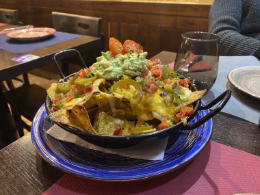 Eritilmiş peynir soslu, biberli, biberli, kırmızı soğanlı, domatesli, siyah zeytinli, salsa soslu ve ekşi kremalı lezzetli tortilla naçosu. Bir restoranda.