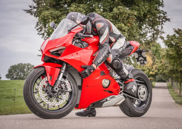 Ducati Panigale V4. Dainese takım elbiseli bir motosikletçi motosikletine sarılıyor.