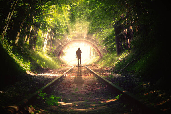 The guy stands at the entrance to the tunnel from which the light shines.