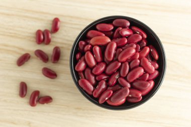 Ahşap arka planda siyah bir kasede kırmızı böbrek fasulyesi, üst manzara, düz uzanma, tepeden aşağı, seçici odak.