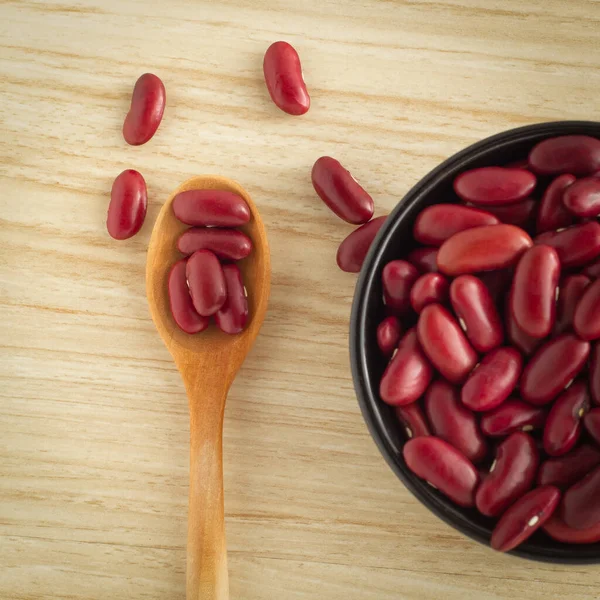 red kidney beans in a wood spoon and black bowl on wooden background, top view, flat lay, top-down, selective focus.
